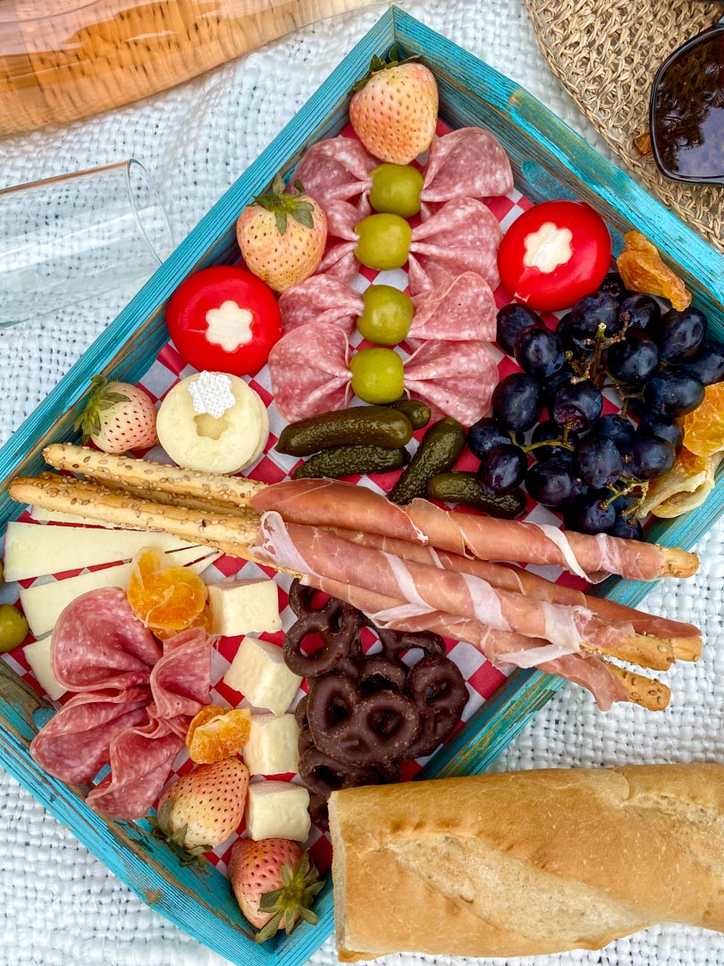 charcuterie board on a white blanket with a bottle of wine on the side