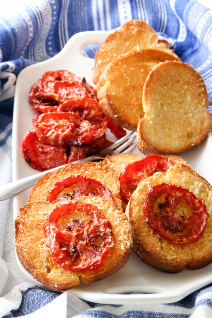 white platter with toast topped with roasted tomatoes