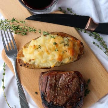 twice baked potato, steak on a cutting board. Glass of red wine on the side