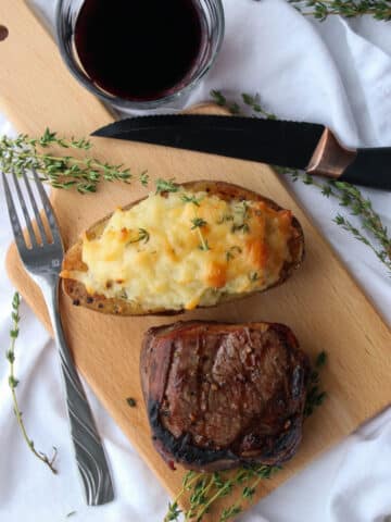 twice baked potato, steak on a cutting board. Glass of red wine on the side