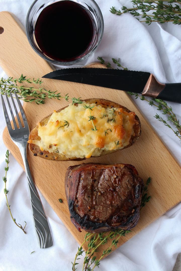 twice baked potato, steak on a cutting board. Glass of red wine on the side