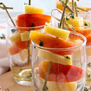 small appetizer glasses filled with peaches and gouda cheese on skewers