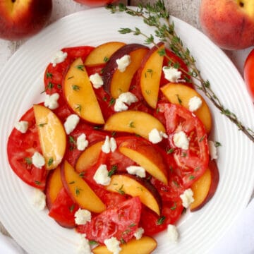 white plate with sliced peaches, tomatoes, goat cheese and thyme