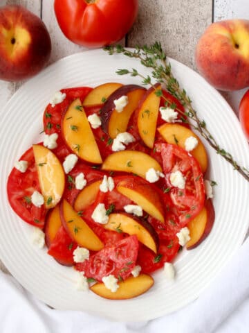 white plate with sliced peaches, tomatoes, goat cheese and thyme