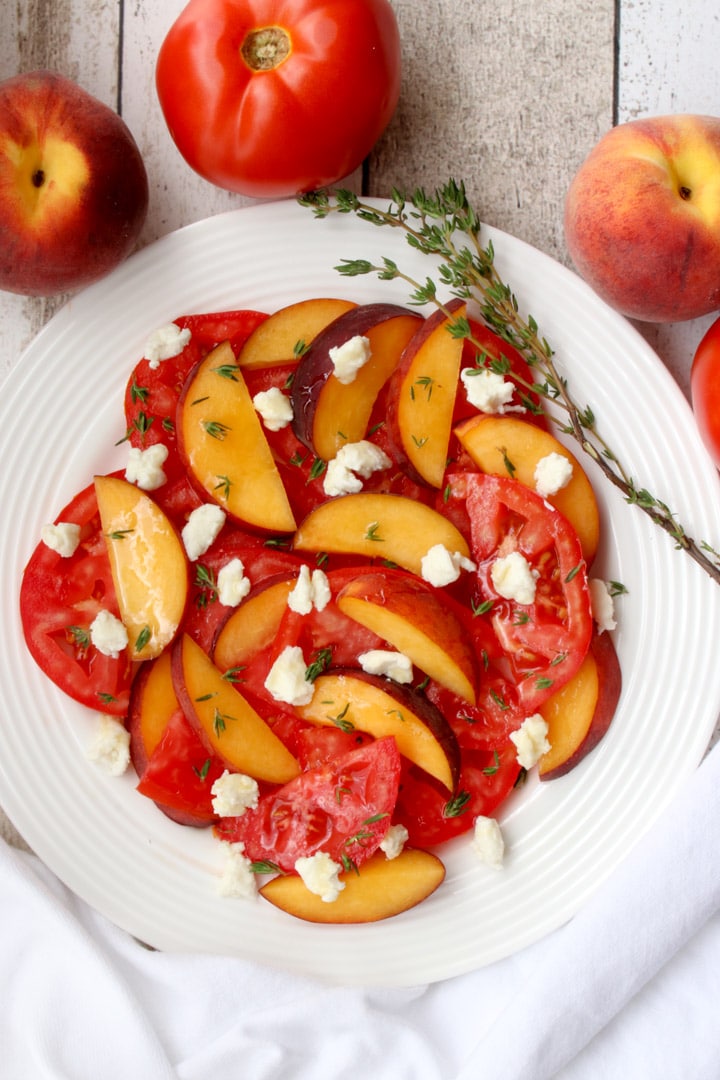 white plate with sliced peaches, tomatoes, goat cheese and thyme