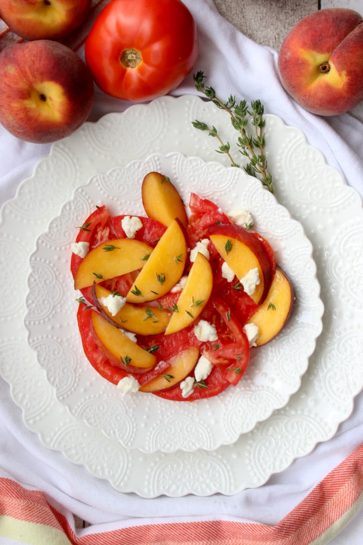 white plate with sliced peaches, tomatoes, goat cheese and thyme