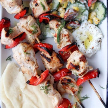 Chicken Kabobs on a white platter with cucumber salad