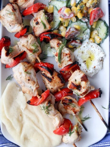 Chicken Kabobs on a white platter with cucumber salad