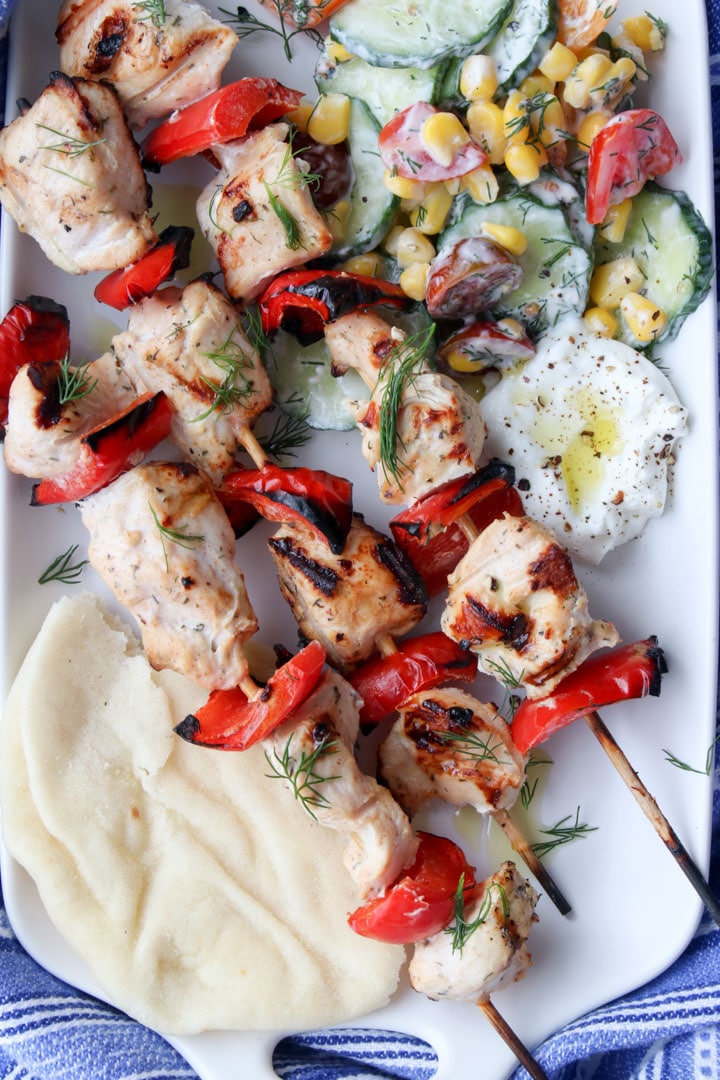 Chicken Kabobs on a white platter with cucumber salad