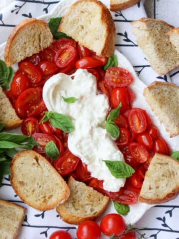 platter of roasted tomatoes, burrata cheese, toasted baguette slices, and fresh basil