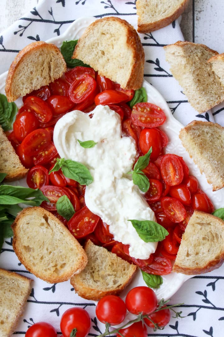 platter of roasted tomatoes, burrata cheese, toasted baguette slices, and fresh basil