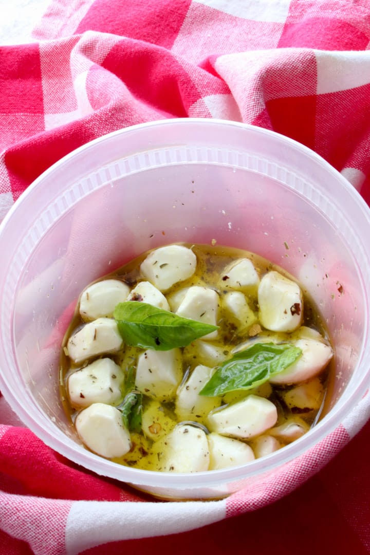 plastic container with mozzarella pearls, olive oil, and herbs