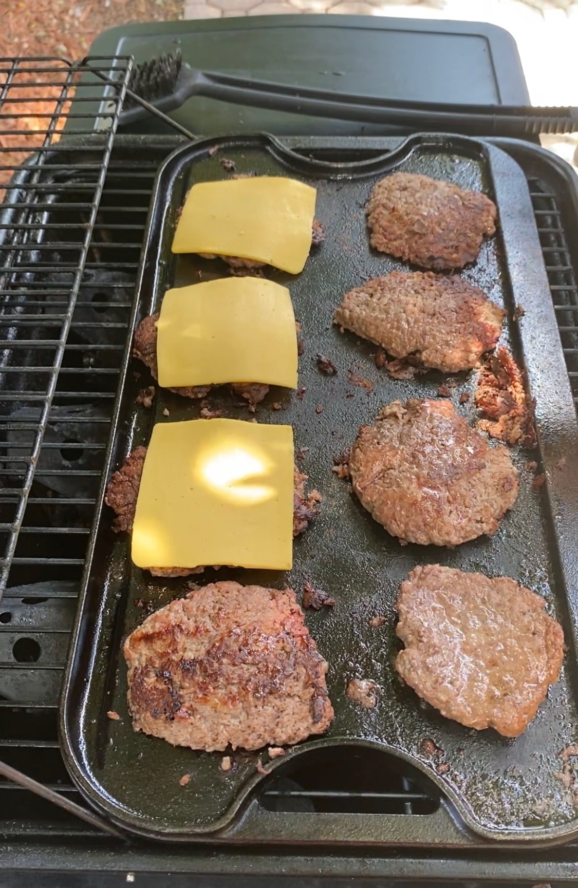 8 burgers on a grill. 3 topped with American cheese