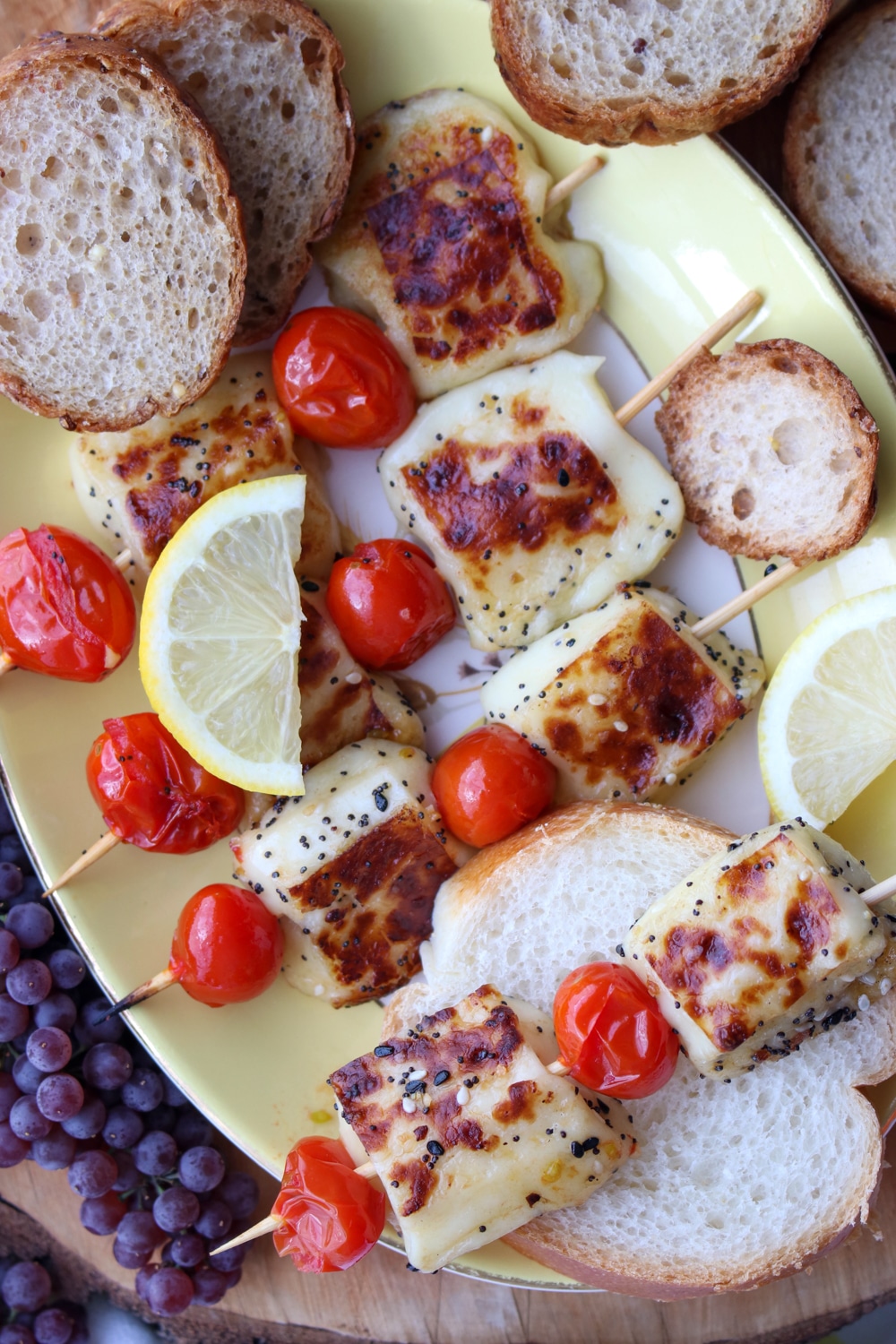 Grilled cheese and tomato skewers on a plate with bread slices and lemon slices.