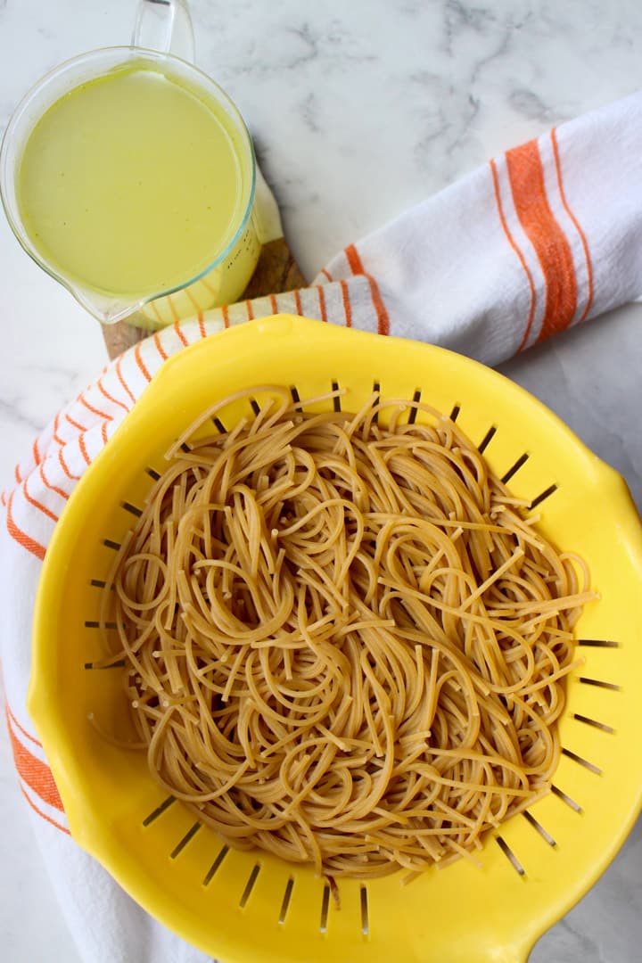 bowl of cooked pasta with a cup of pasta water on the side