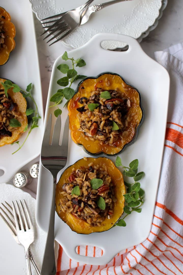 white plate with 2 slices of acorn squash stuffed with wild rice