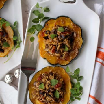 white plate with 2 slices of acorn squash stuffed with wild rice