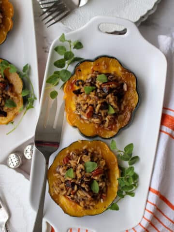 white plate with 2 slices of acorn squash stuffed with wild rice