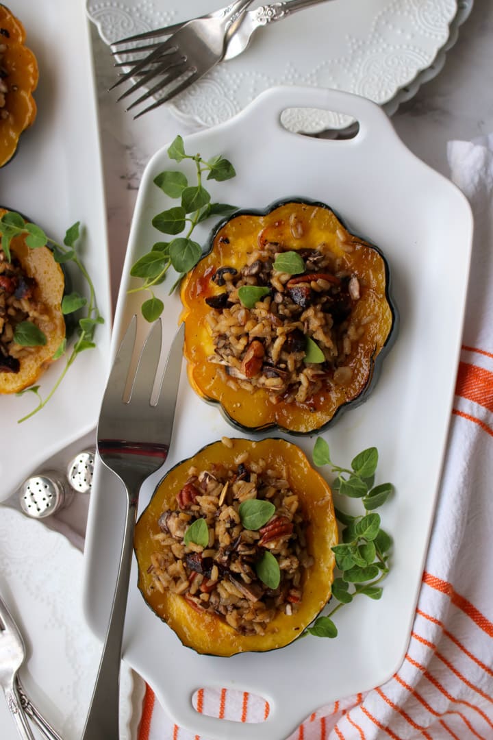 white plate with 2 slices of acorn squash stuffed with wild rice