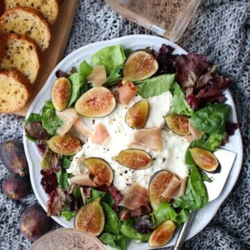 platter of burrata cheese, mixed greens, and sliced figs with toast crisps and champaign