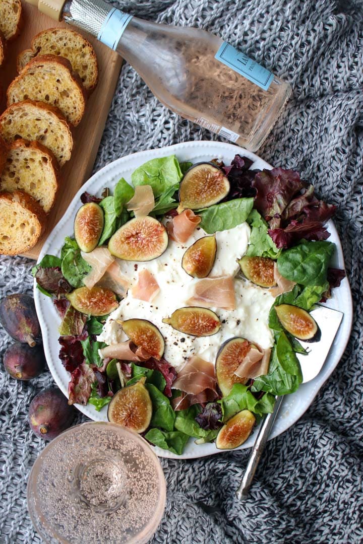 platter of burrata cheese, mixed greens, and sliced figs with toast crisps and champaign