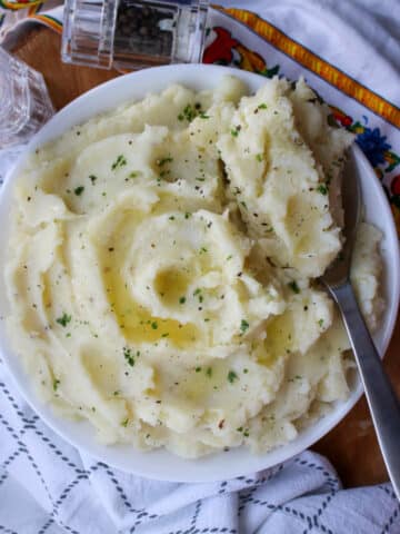 large bowl of mashed potatoes with butter and parsley with a large serving spoon