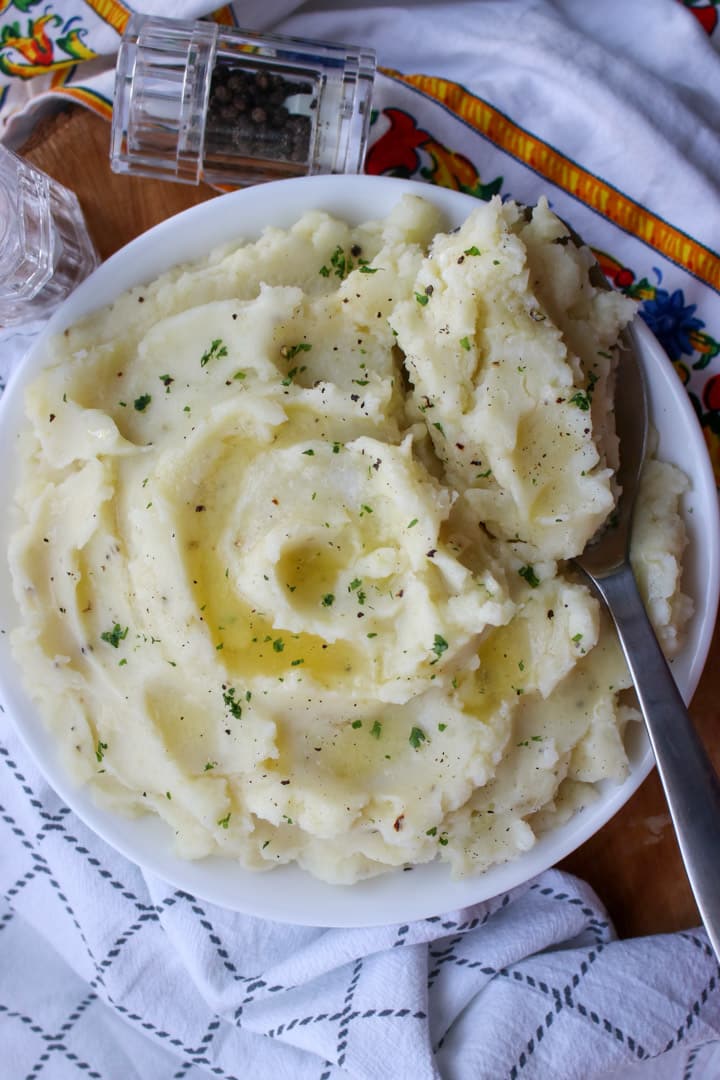 large bowl of mashed potatoes with butter and parsley with a large serving spoon