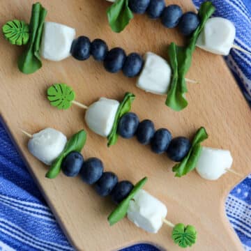 four blueberry caprese skewers on a small board