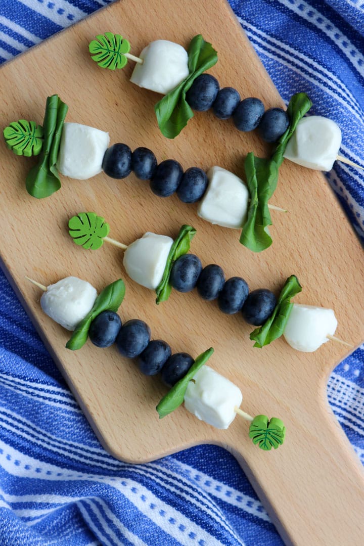 four blueberry caprese skewers on a small board