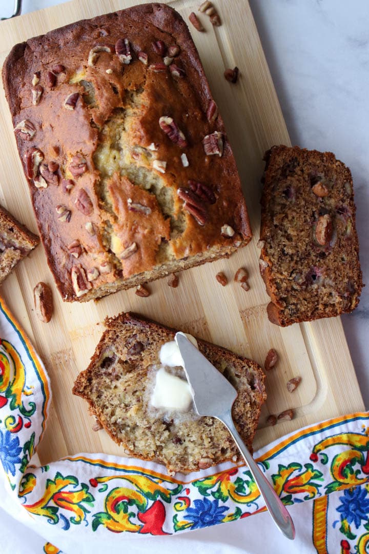 overhead shot of loaf of banana bread with a slice on it's side with melting butter