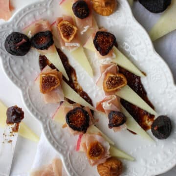 white platter of sliced manchego cheese with figs and prosciutto