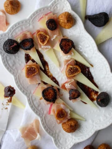 white platter of sliced manchego cheese with figs and prosciutto