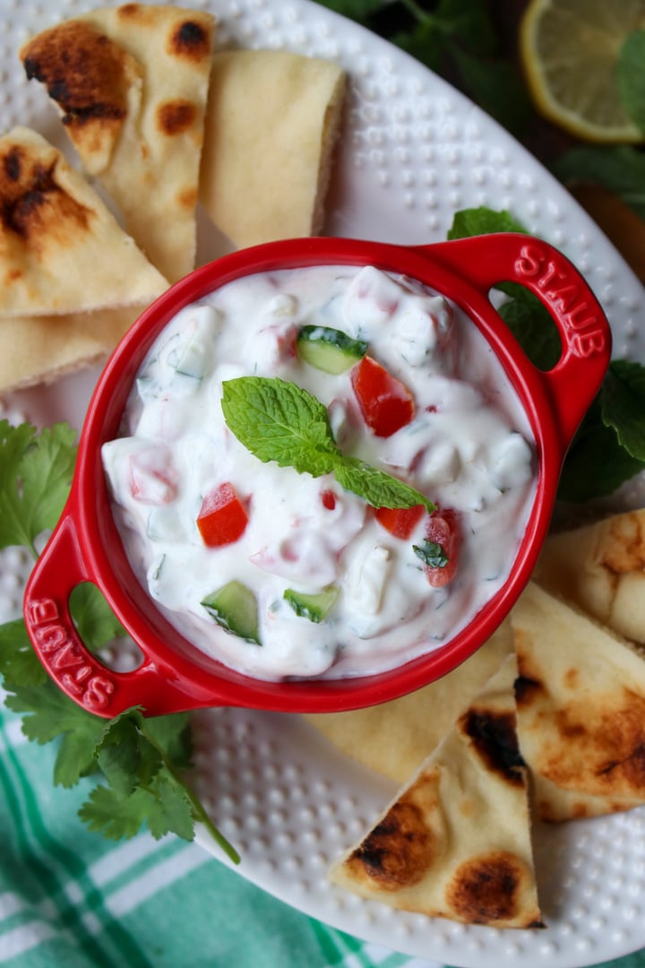 red bowl filled with raita surrounded by pita chips