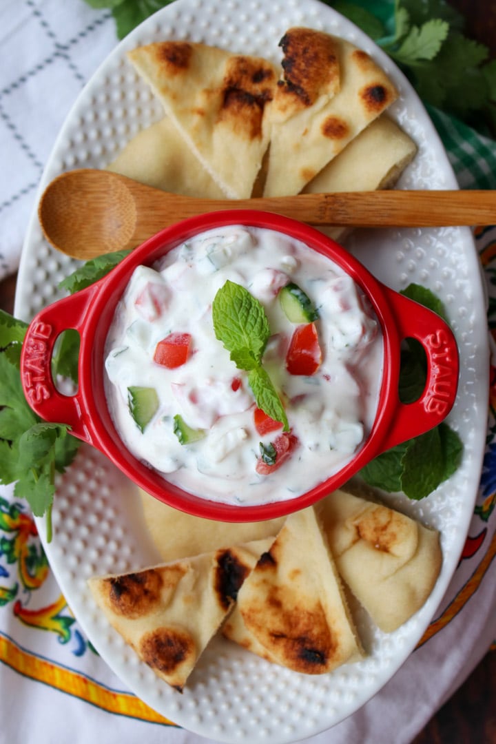 red bowl filled with raita on a white plate with pita chips