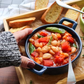 woman's hand reaching for a blue bowl filled with white bean tomato soup