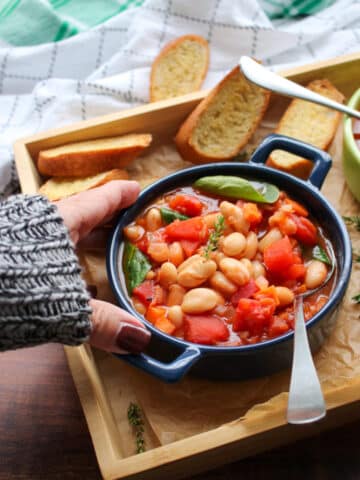 woman's hand reaching for a blue bowl filled with white bean tomato soup