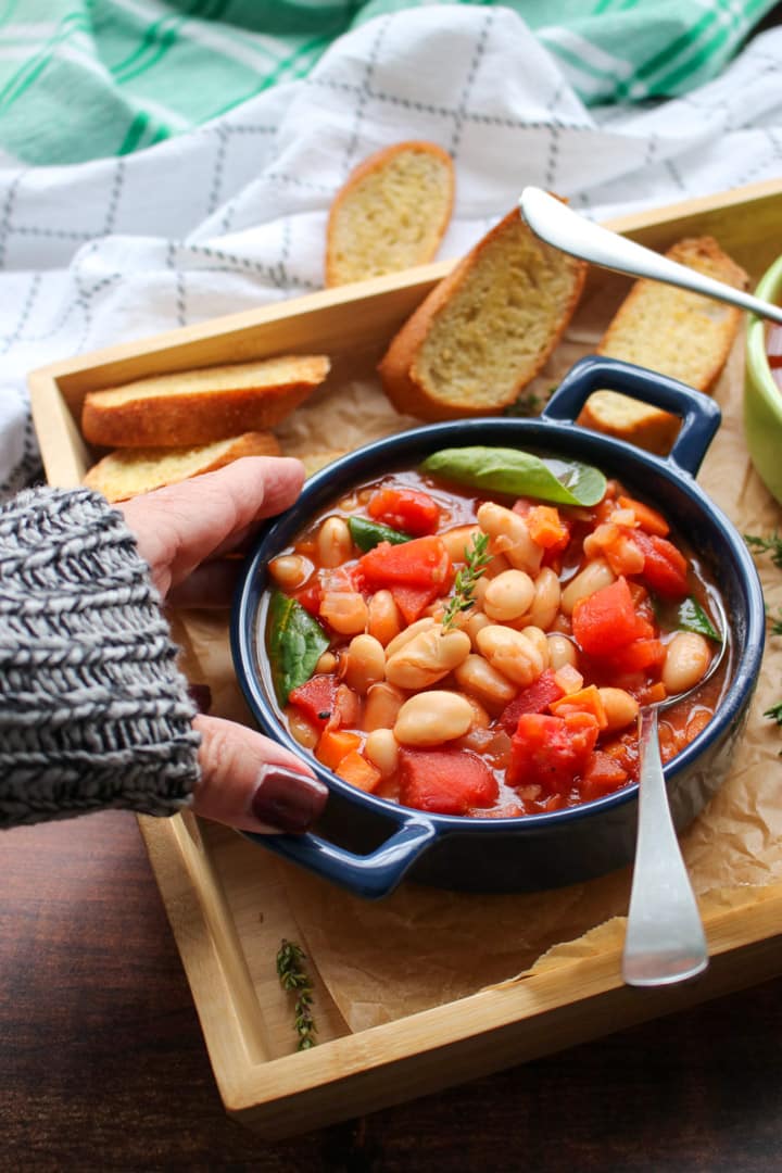 woman's hand reaching for a blue bowl filled with white bean tomato soup