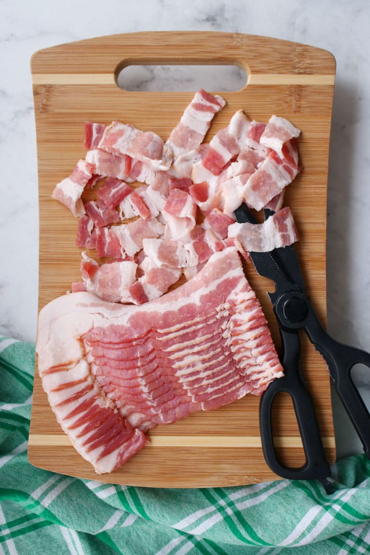 bacon being slice with a scissors on a cutting board