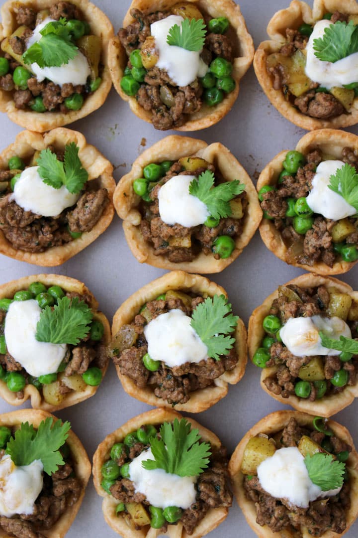 Mini beef pies in a row on a cooking sheet