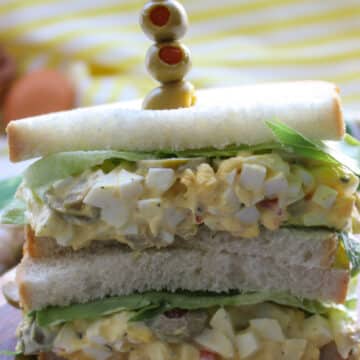 egg salad sandwich with a skewer of green olives stuck into it