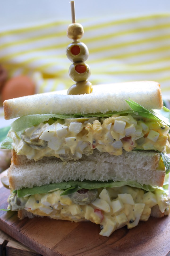 egg salad sandwich with a skewer of green olives stuck into it