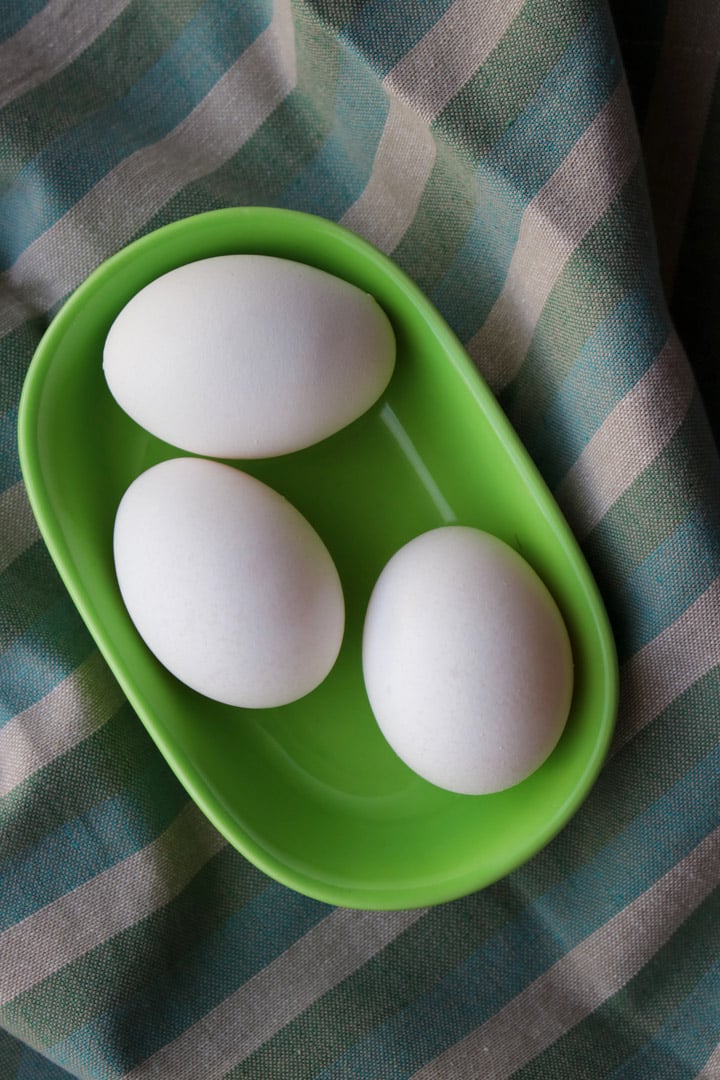 three white eggs in a green dish with a green striped dish towel