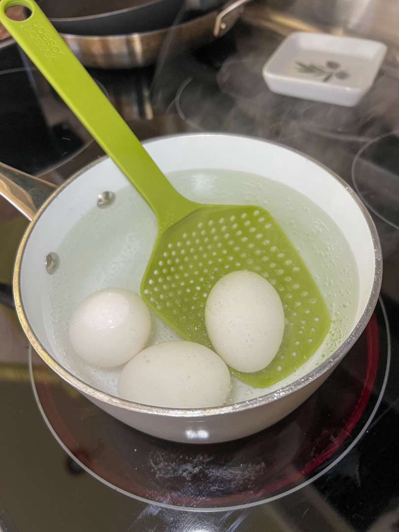 three eggs in a sauce pan filled with water on the stove