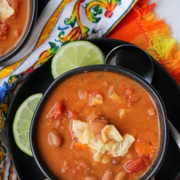 Pinto bean soup in a black bowl garnished with tortilla chips and lime slices