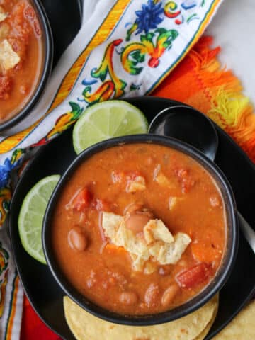 Pinto bean soup in a black bowl garnished with tortilla chips and lime slices