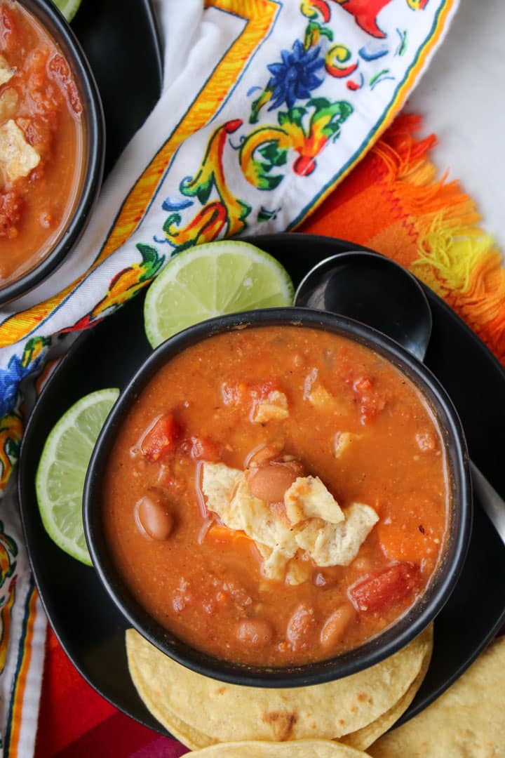 Pinto bean soup in a black bowl garnished with tortilla chips and lime slices