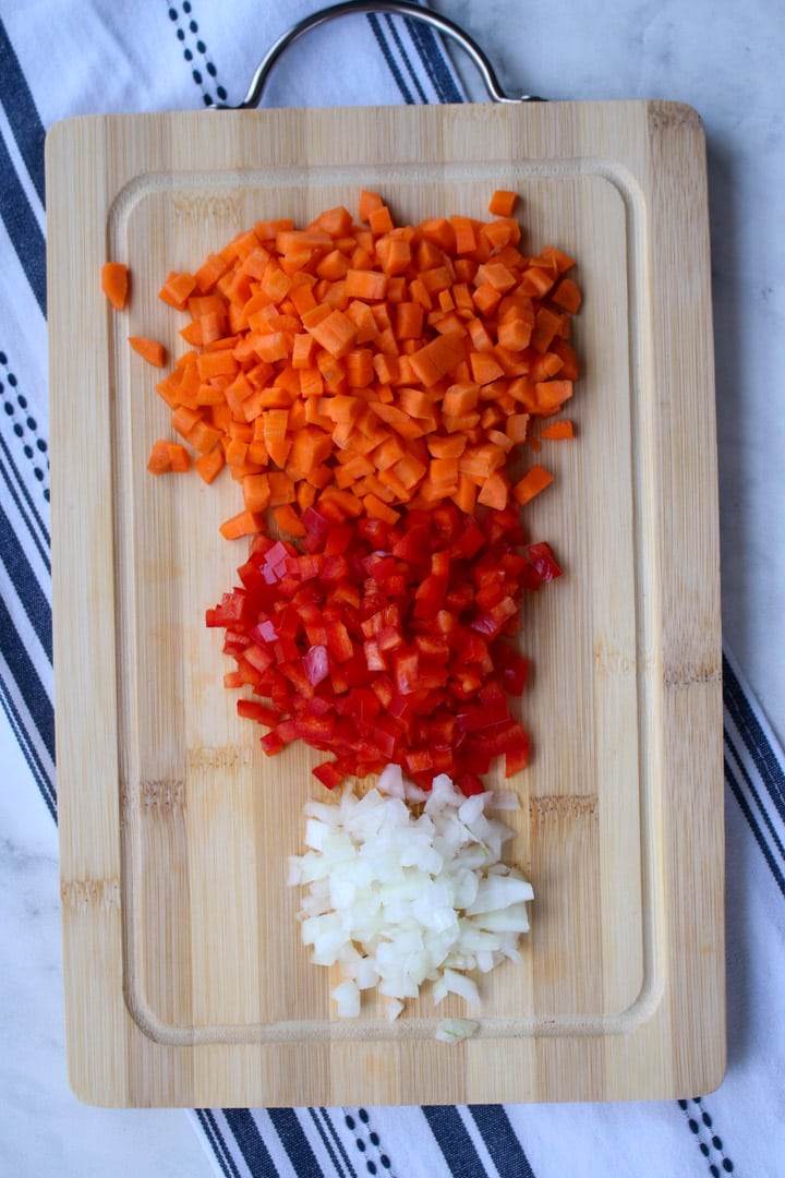 chopped carrots, red bell pepper, and onion diced and sitting in piles on a cutting board