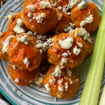 Pile of buffalo chicken meatballs topped with blue cheese with celery stick on the side