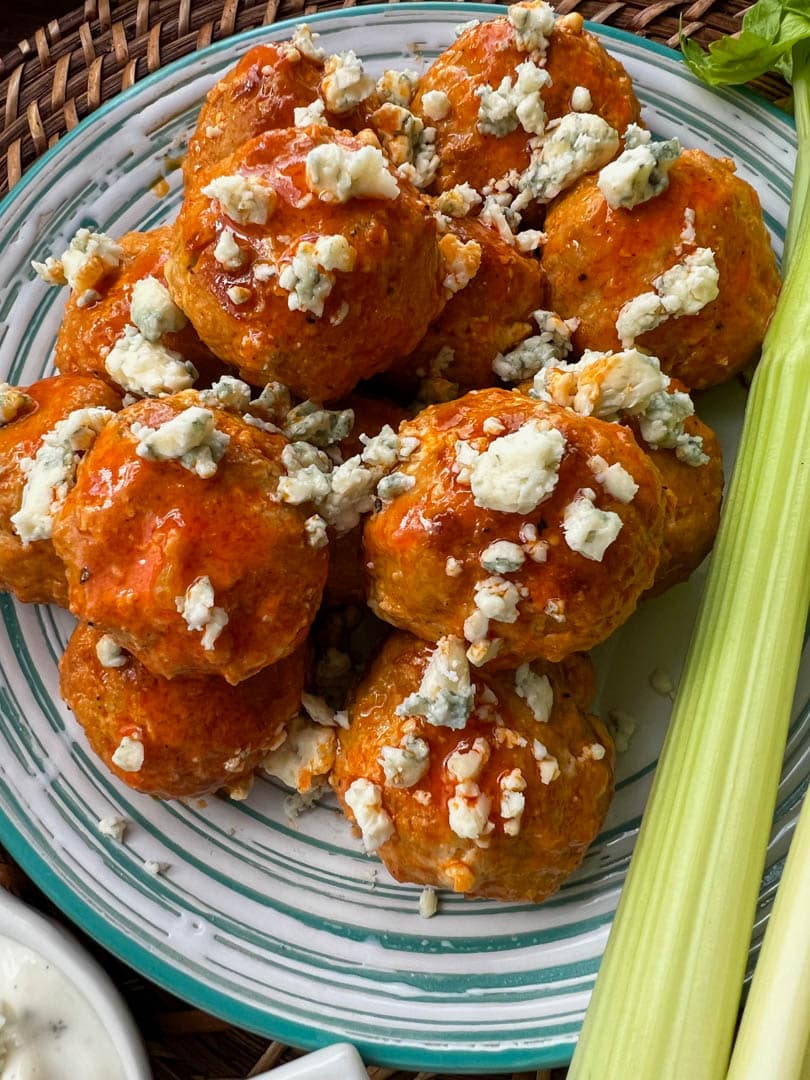 Pile of buffalo chicken meatballs topped with blue cheese with celery stick on the side