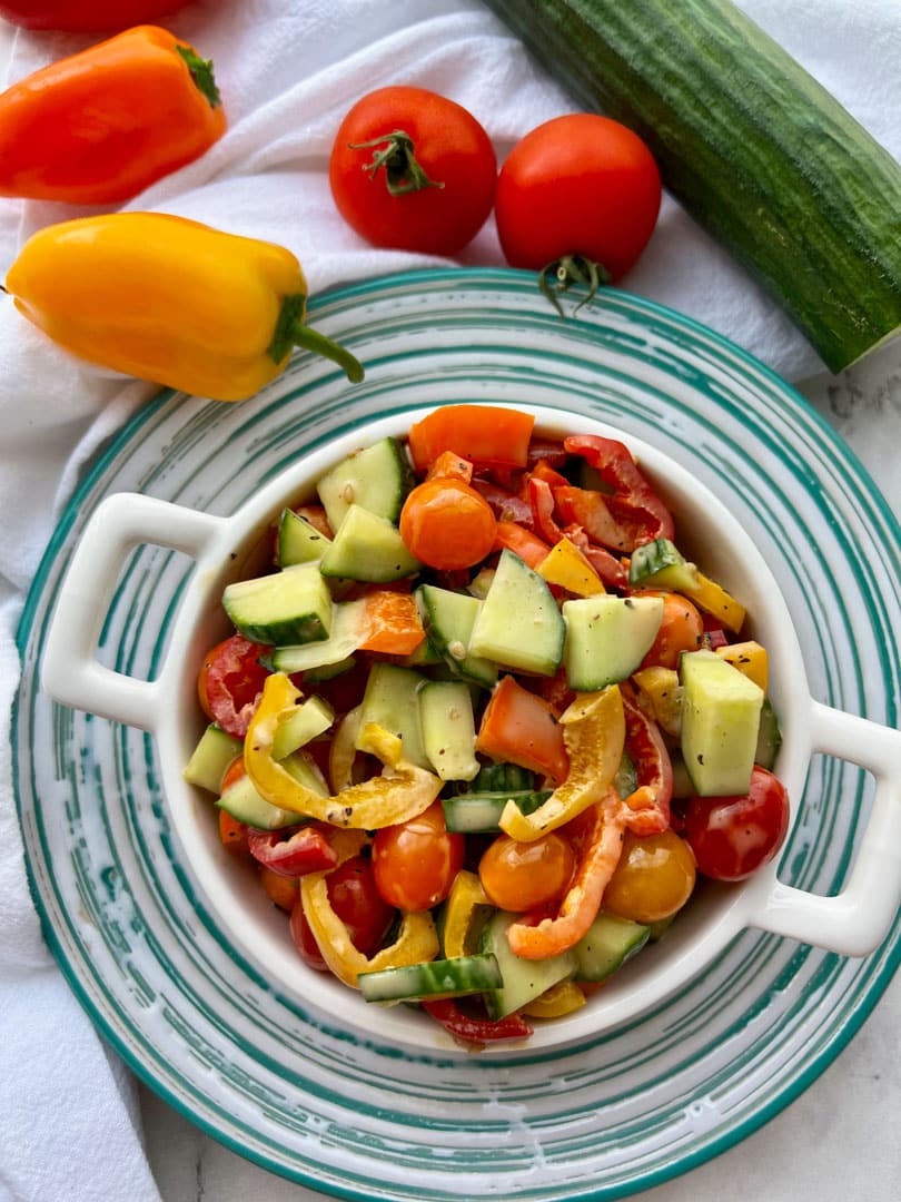 cucumber pepper salad in a bowl surrounded by mini peppers